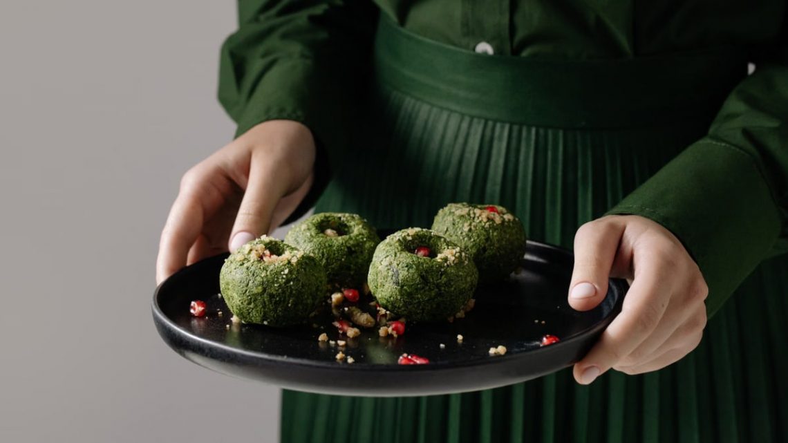 Delicious Georgian spinach pkhali on a black plate, held by a person in green attire.